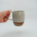 Kleybird Strata mug held in hand, showing marbled clay bottom and white speckled glaze top.