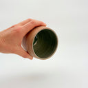 Kleybird Strata handleless tumbler with marbled clay exterior and light aqua interior held in hand.