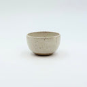 Small rounded ceramic bowl used for sake or espresso, featuring a speckled white glaze and held in a hand for scale.